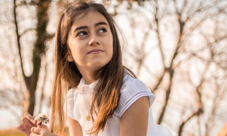 Ragazza in abito bianco con fiori, seduta all'aperto.