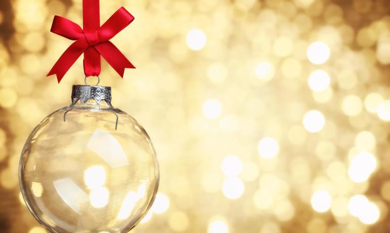 Palla di Natale trasparente con nastro rosso su sfondo dorato.