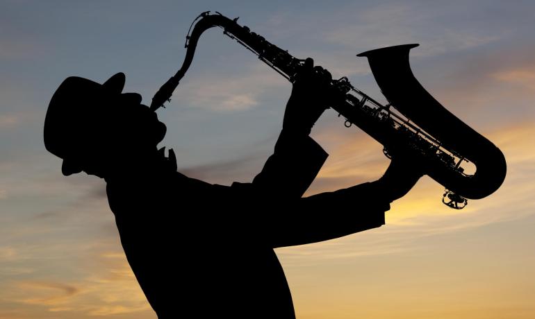 Sagoma di un musicista che suona il sassofono al tramonto.
