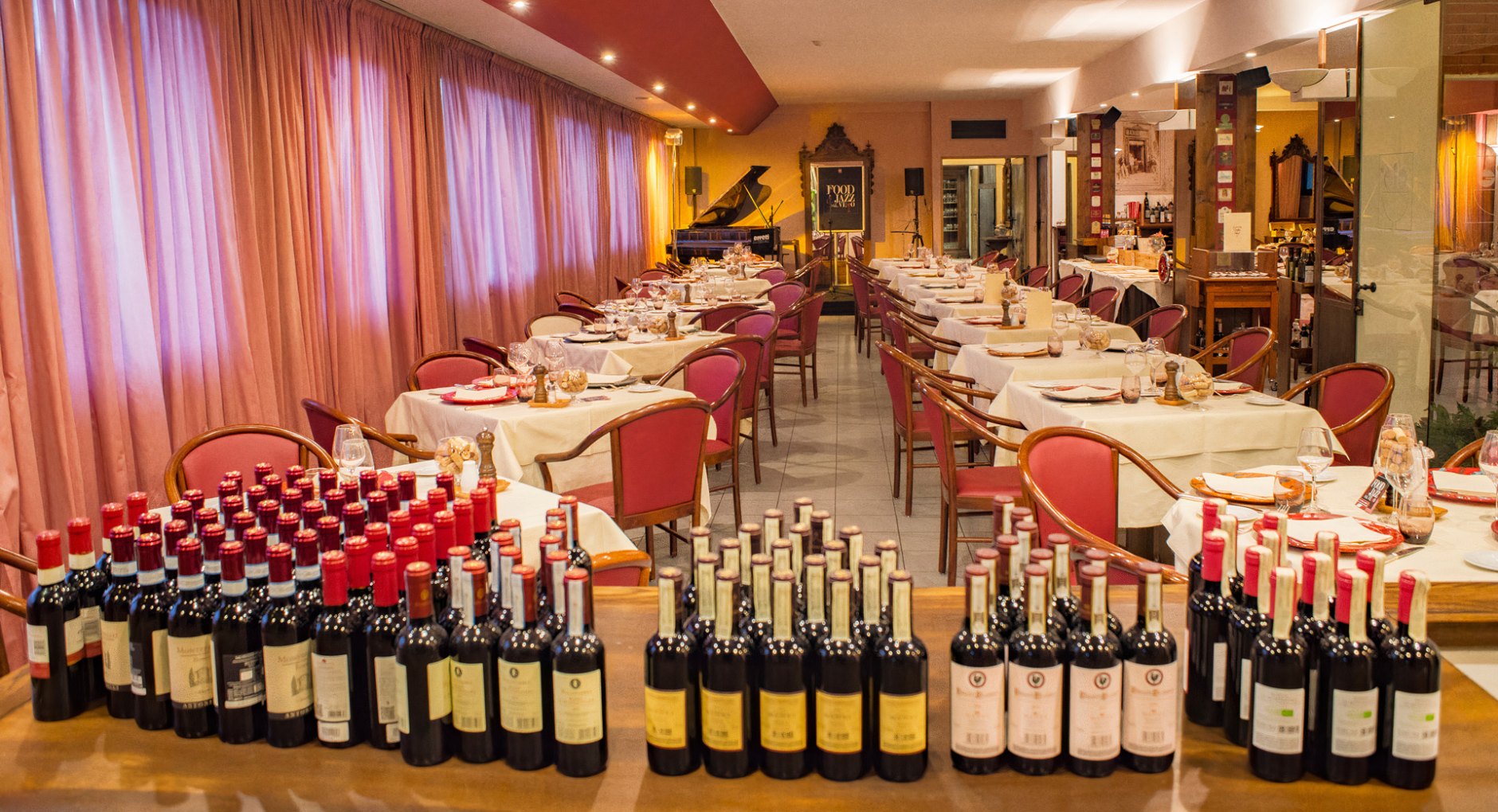 Ristorante elegante, tavoli apparecchiati, bottiglie di vino, atmosfera calda e accogliente.