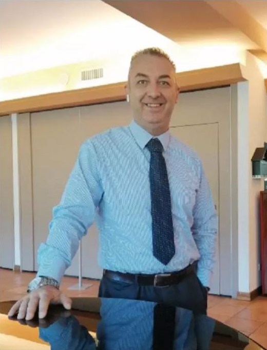 Uomo in camicia e cravatta, sorridente, in un ambiente interno elegante.
