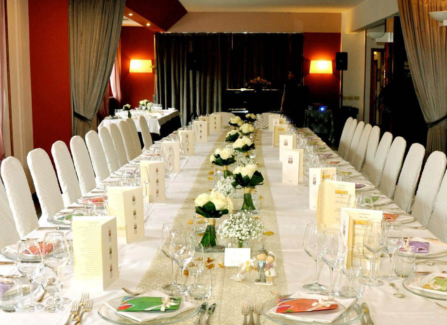 Tavola elegante apparecchiata per un evento, con fiori bianchi e menù su ogni posto.