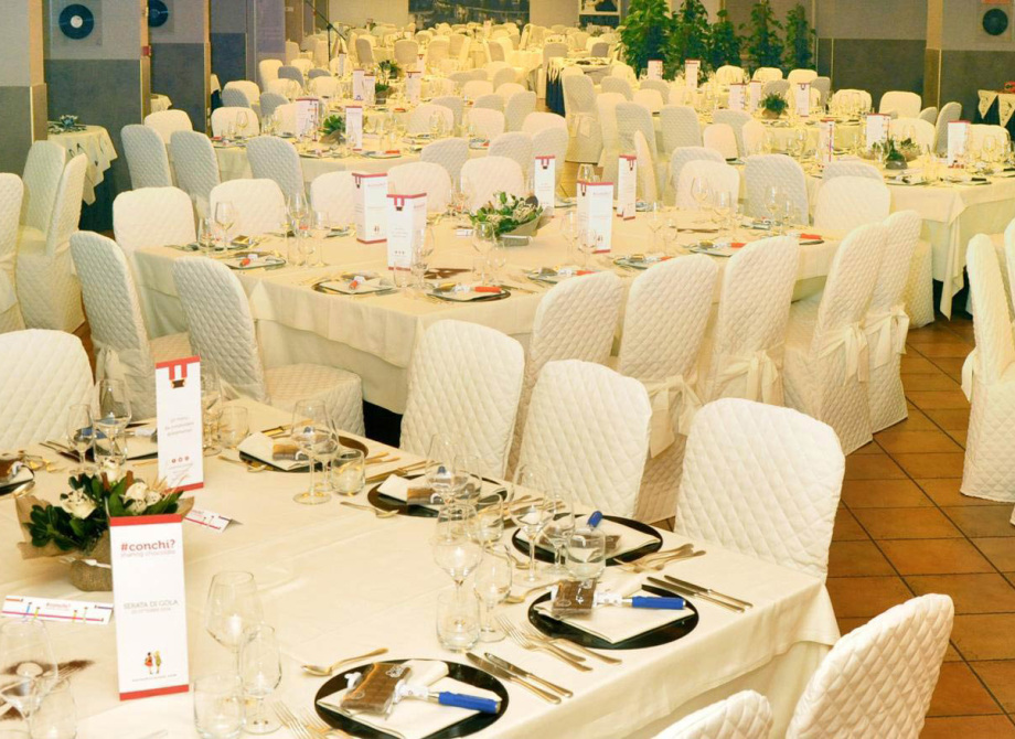 Sala ricevimenti elegante con tavoli apparecchiati e sedie coperte di bianco.