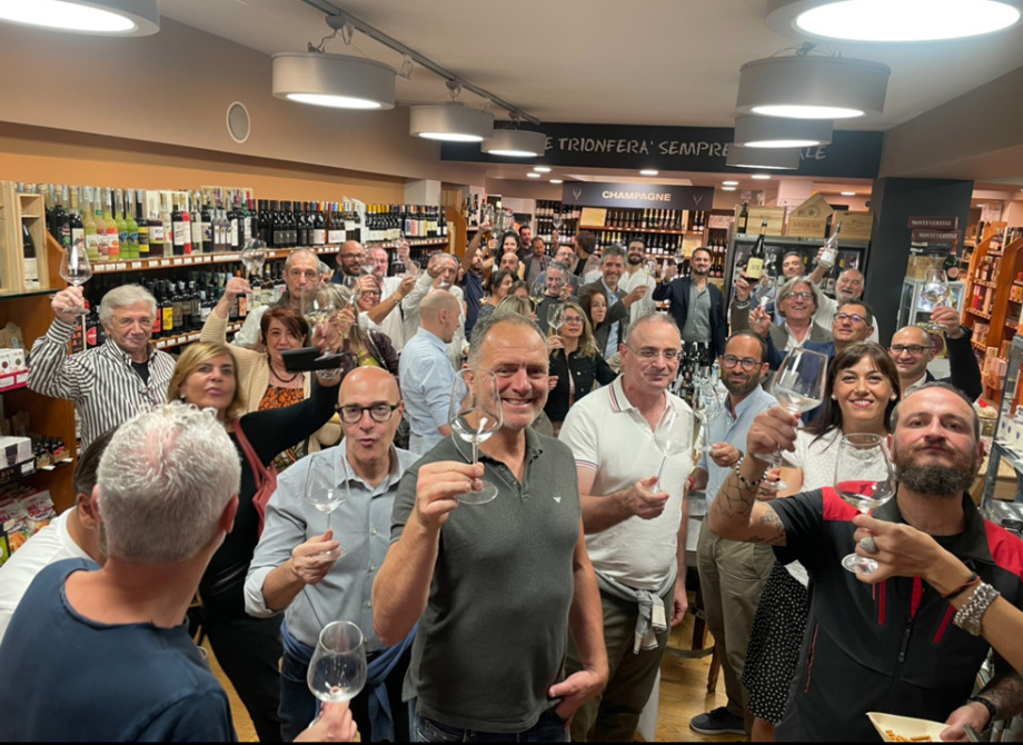 Gruppo di persone brinda in un negozio di vini, atmosfera festosa e conviviale.