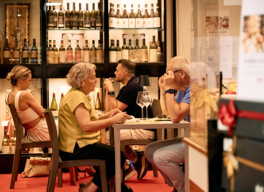 Personnes dans un bar à vin, ambiance intime, conversations animées, verres de vin.