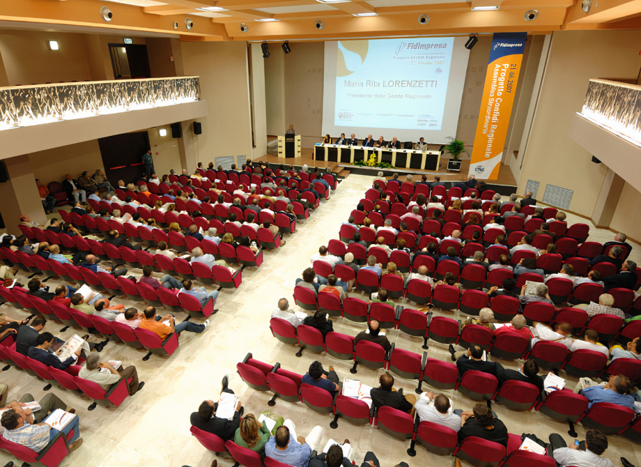 Conferenza in auditorium con pubblico seduto e presentazione sul palco.