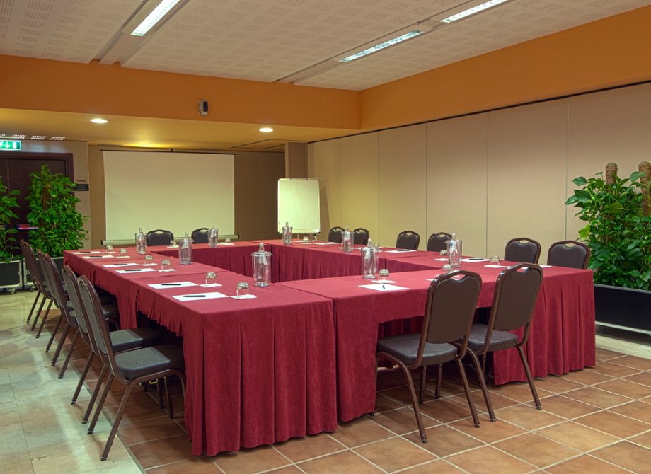 Sala riunioni con tavoli a U, sedie e attrezzature per conferenze.