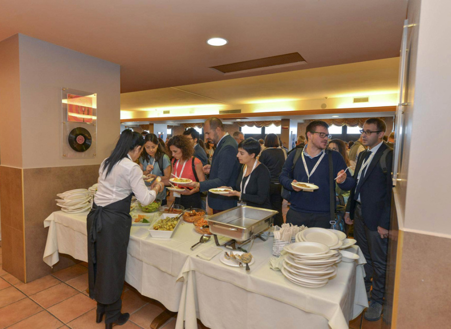 Persone in fila per il buffet a un evento, con piatti e cibo esposti.