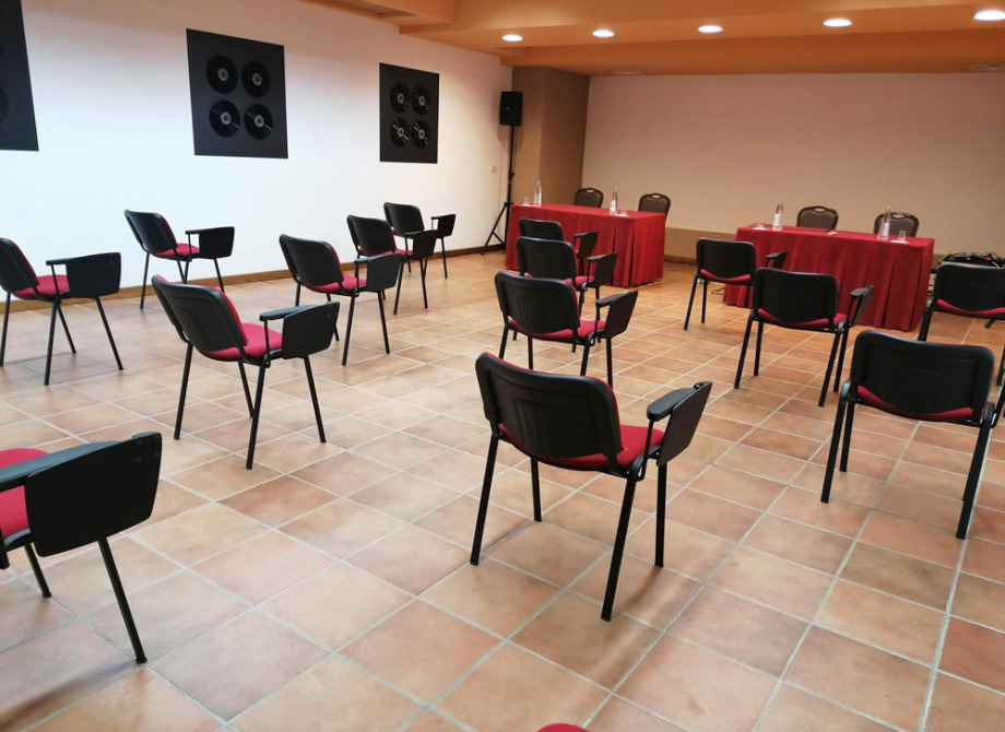 Sala conferenze con sedie distanziate e tavoli con tovaglie rosse.