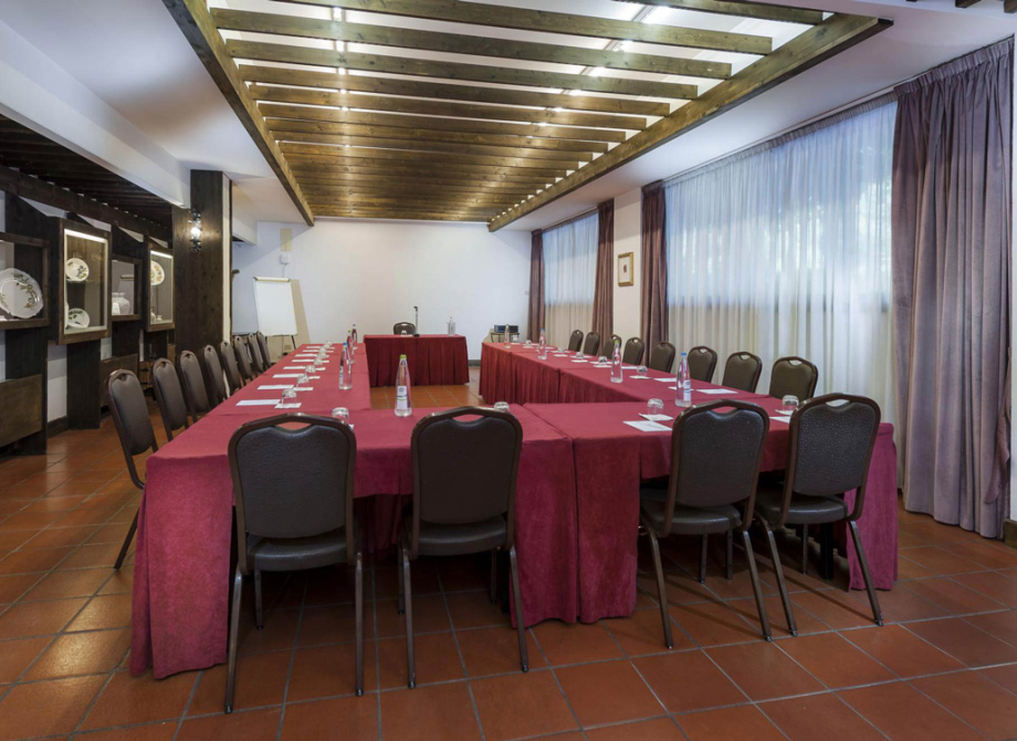 Sala riunioni con tavoli a U, sedie, bottiglie d'acqua e blocchi per appunti.