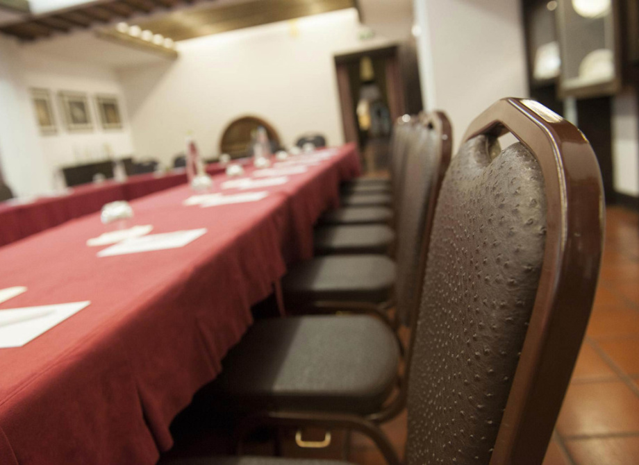 Sala conferenze con tavolo coperto e sedie in fila, atmosfera formale.