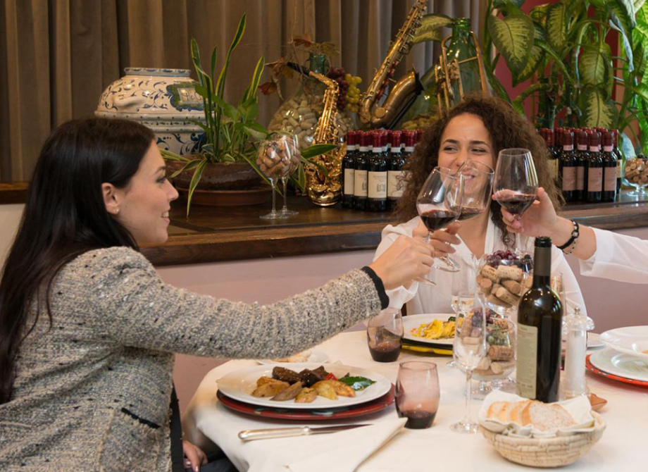 Tre donne brindano a tavola in un ristorante con vino e cibo.