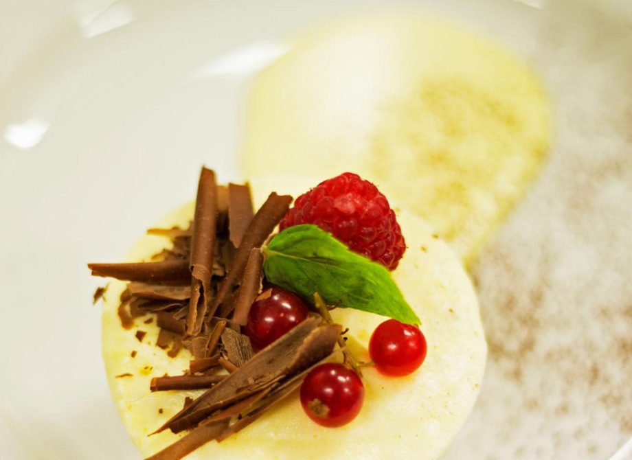 Dessert elegante con cioccolato, lamponi e ribes, decorato con foglie verdi su piatto bianco.