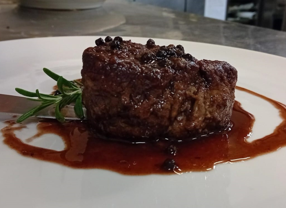 Filetto di carne con salsa al pepe e rametto di rosmarino su piatto bianco.