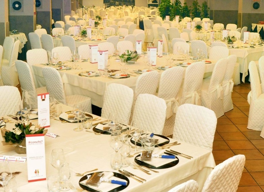 Sala da ricevimento elegante con tavoli apparecchiati e sedie rivestite di bianco.