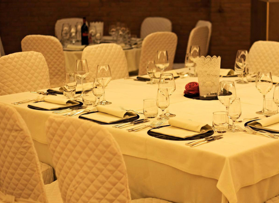 Tavola elegante apparecchiata per una cena, con tovaglie bianche e sedie imbottite.