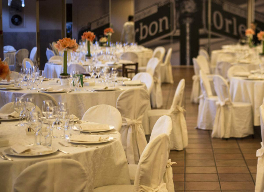Sala ricevimenti elegante con tavoli apparecchiati e fiori arancioni.