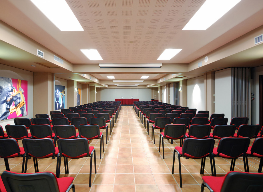 Sala conferenze con sedie rosse e nere, decorata con immagini di musicisti.