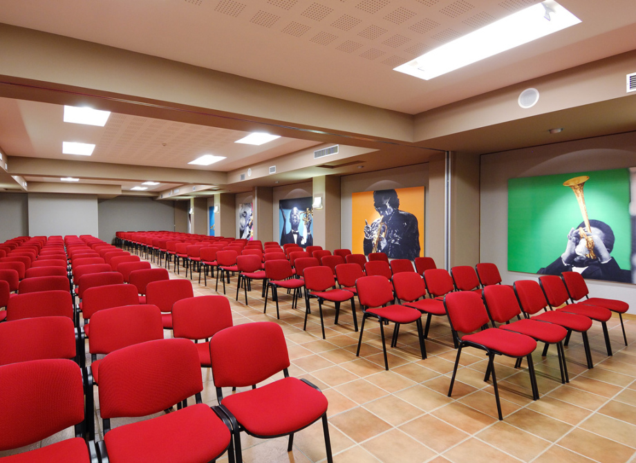 Sala conferenze con sedie rosse e poster colorati di musicisti jazz alle pareti.