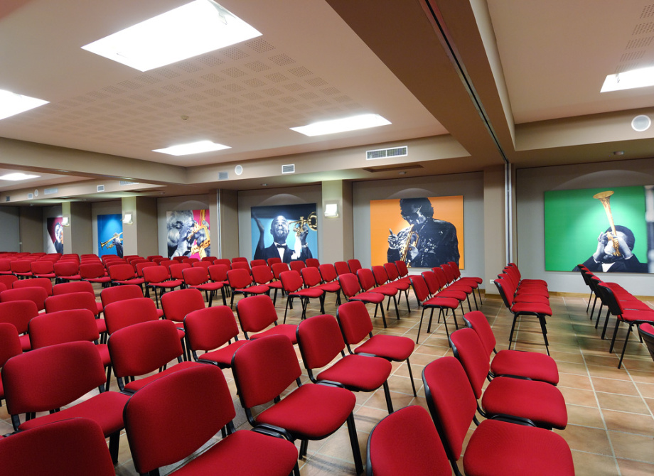 Sala conferenze con sedie rosse e ritratti di musicisti jazz alle pareti.