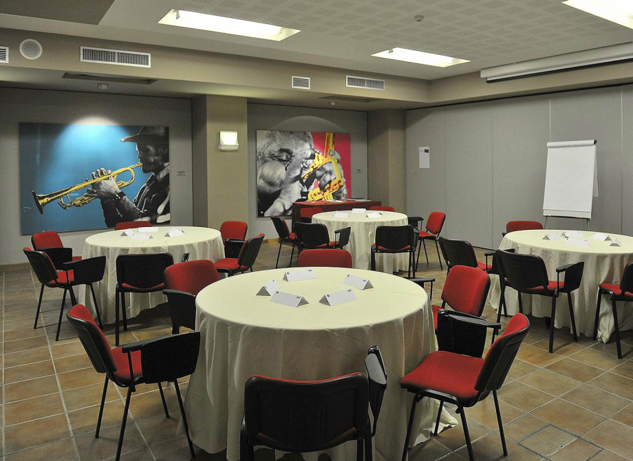 Sala conferenze con tavoli rotondi, sedie rosse e decorazioni musicali alle pareti.